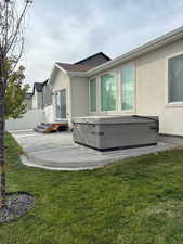 Rear view of house featuring stucco siding, a lawn, a patio area, and a hot tub