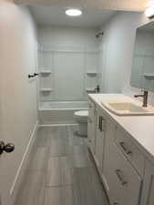 Bathroom featuring tub / shower combination, vanity, a textured ceiling, and wood finish floors