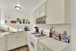 Kitchen with open shelves, white range with gas stovetop, light countertops, and light wood finished floors