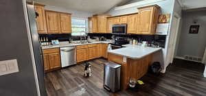 Kitchen with vaulted ceiling, decorative backsplash, stainless steel appliances, dark wood-style floors, and a peninsula