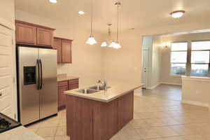 Kitchen featuring stainless steel fridge, brown cabinetry, light tile  floors, light countertops, and recessed lighting
