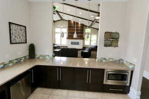 Kitchen featuring vaulted ceiling, a glass covered fireplace, appliances with stainless steel finishes, light stone countertops, and decorative backsplash