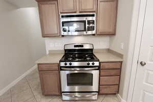Kitchen featuring appliances with stainless steel finishes, light tile floors, and light stone counters