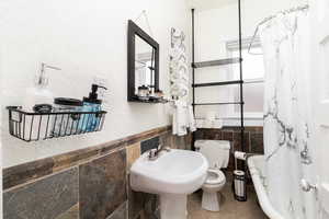 Bathroom featuring tile walls, wainscoting, a textured wall, shower / bath combo, and tile patterned flooring