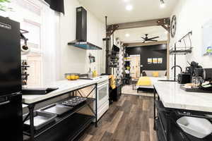 Kitchen with wall chimney range hood, dark wood-type flooring, white range with electric cooktop, freestanding refrigerator, and light stone counters