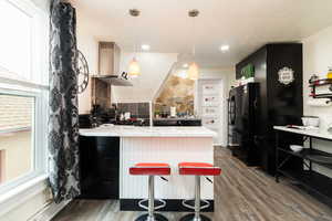 Kitchen with a peninsula, dark wood-type flooring, light countertops, ventilation hood, and freestanding refrigerator