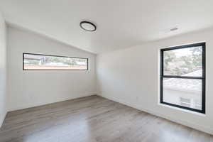 Spare room with light wood-type flooring and vaulted ceiling