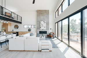 Living room with a high ceiling, wood finished floors, a tiled fireplace, and a ceiling fan