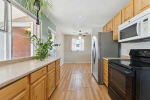 Kitchen featuring black range with electric stovetop, white microwave, light wood-look vinyl flooring, light countertops, and a ceiling fan