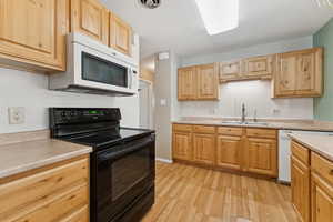 Kitchen featuring white appliances, light wood-style flooring, light countertops, light brown cabinetry, and backsplash