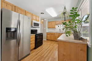 Kitchen with stainless steel refrigerator with ice dispenser, electric range, light brown cabinets, light wood-style flooring, and light countertops
