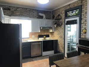 Kitchen with stainless steel appliances, light countertops, exposed brick wall, crown molding, and vented range hood. Stained glass transom.