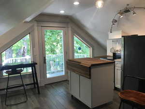 Kitchen with wood counters, appliances with stainless steel finishes, dark wood-type flooring, a kitchen island, and lofted ceiling