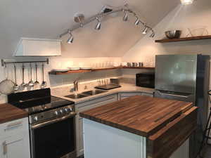 Kitchen with wooden counters, open shelves, appliances with stainless steel finishes, track lighting, and lofted ceiling