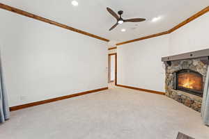 Unfurnished living room featuring a stone fireplace, ceiling fan, ornamental molding, carpet flooring, and recessed lighting