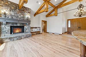 Unfurnished living room with high vaulted ceiling, beam ceiling, wood finished floors, a fireplace, and a chandelier
