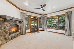 Unfurnished living room with plenty of natural light, a stone fireplace, carpet flooring, and crown molding