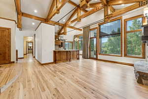 Unfurnished living room featuring a chandelier, beamed ceiling, light wood finished floors, high vaulted ceiling, and recessed lighting