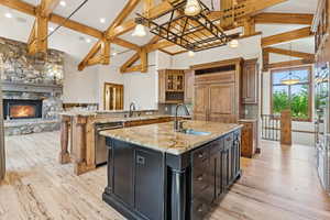 Kitchen featuring backsplash, beamed ceiling, a center island with sink, stainless steel dishwasher, and high vaulted ceiling