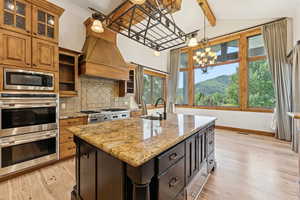 Kitchen with appliances with stainless steel finishes, light wood-style flooring, decorative backsplash, light stone counters, and a kitchen island with sink