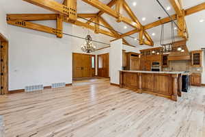 Kitchen featuring high vaulted ceiling, a chandelier, brown cabinets, decorative backsplash, and light wood-style flooring