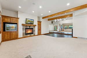 Unfurnished living room featuring beam ceiling, a tiled fireplace, carpet flooring, and recessed lighting
