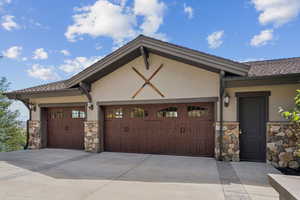 View of front of home featuring stone siding, a garage, concrete driveway, and stucco siding
