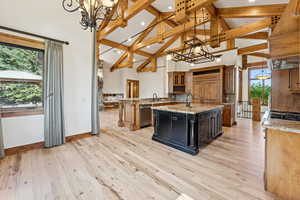 Kitchen with decorative backsplash, an island with sink, high vaulted ceiling, light wood-style floors, and island range hood