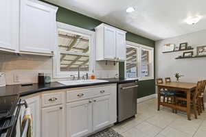 Kitchen with decorative backsplash, dark countertops, stainless steel dishwasher, light tile patterned floors, and white cabinetry