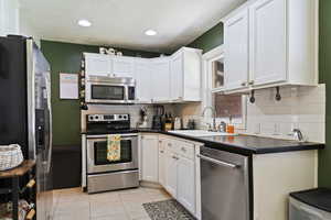 Kitchen featuring appliances with stainless steel finishes, tasteful backsplash, dark countertops, light tile patterned flooring, and white cabinetry