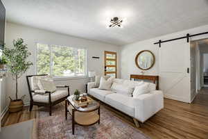 Living room with a barn door, wood finished floors, and a textured ceiling