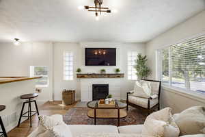 Living area featuring wood finished floors, plenty of natural light, a fireplace, a textured ceiling, and a chandelier