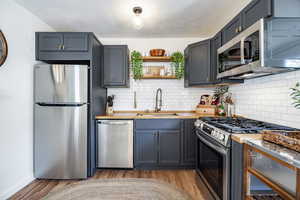Kitchen featuring stainless steel appliances, decorative backsplash, light wood-style floors, and open shelves