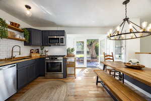 Kitchen featuring appliances with stainless steel finishes, backsplash, open shelves, a chandelier, and light wood-style floors