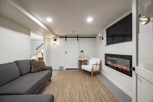 Living room featuring a glass covered fireplace, stairway, finished concrete flooring, and a barn door