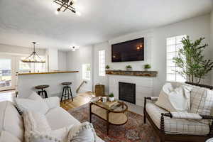 Living room with a chandelier, plenty of natural light, wood finished floors, and a glass covered fireplace