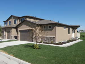 View of front of property with stone siding, stucco siding, a garage, and a front lawn