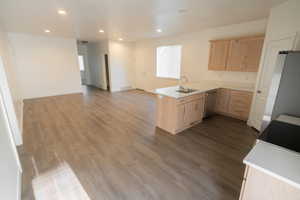 Kitchen featuring light brown cabinetry, open floor plan, a peninsula, dark wood-style floors, and recessed lighting