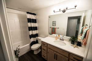 Bathroom with a textured ceiling, wood finished floors, vanity, and shower / bathtub combination with curtain