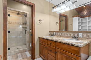 Bathroom with decorative backsplash, a shower stall, double vanity, and tile patterned floors