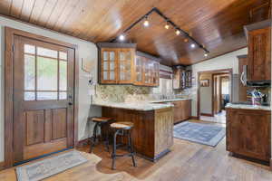 Kitchen with rail lighting, backsplash, a peninsula, light wood finished floors, and light stone countertops