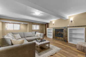 Living room with a fireplace, light wood-style floors, beam ceiling, and built in shelves