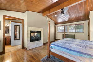 Bedroom featuring wood finished floors, a multi sided fireplace, wooden ceiling, and ceiling fan