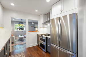 Kitchen featuring appliances with stainless steel finishes, backsplash, dark wood-type flooring, wall chimney exhaust hood, and white cabinetry