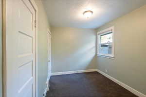 Empty room featuring a textured ceiling and dark colored carpet
