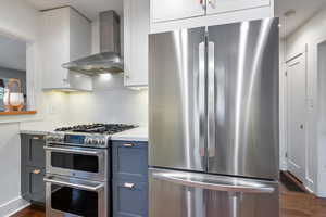 Kitchen featuring stainless steel appliances, wall chimney exhaust hood, dark wood-style flooring, and white cabinets