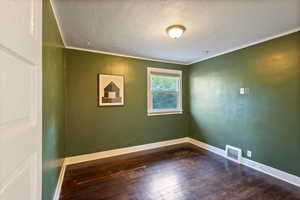 Spare room featuring wood-type flooring, a textured ceiling, and ornamental molding