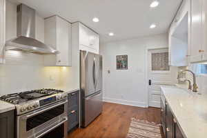 Kitchen featuring backsplash, appliances with stainless steel finishes, wall chimney exhaust hood, light stone countertops, and recessed lighting