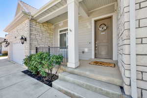 Entrance to property with an attached garage, driveway, a porch, and stone finish