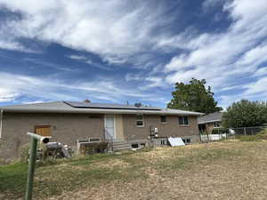 Rear view of house with brick siding, solar panels, and entry steps